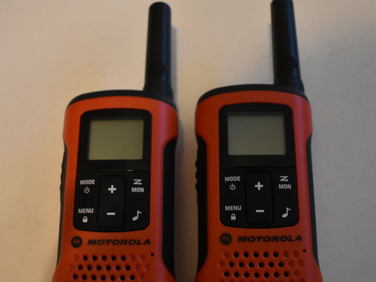 Two handheld radios on a kitchen table beside a flashlight