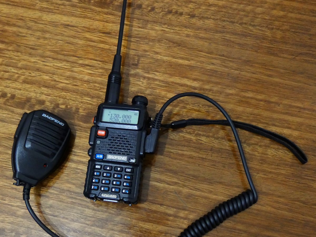 A handheld ham radio on a table beside a notebook